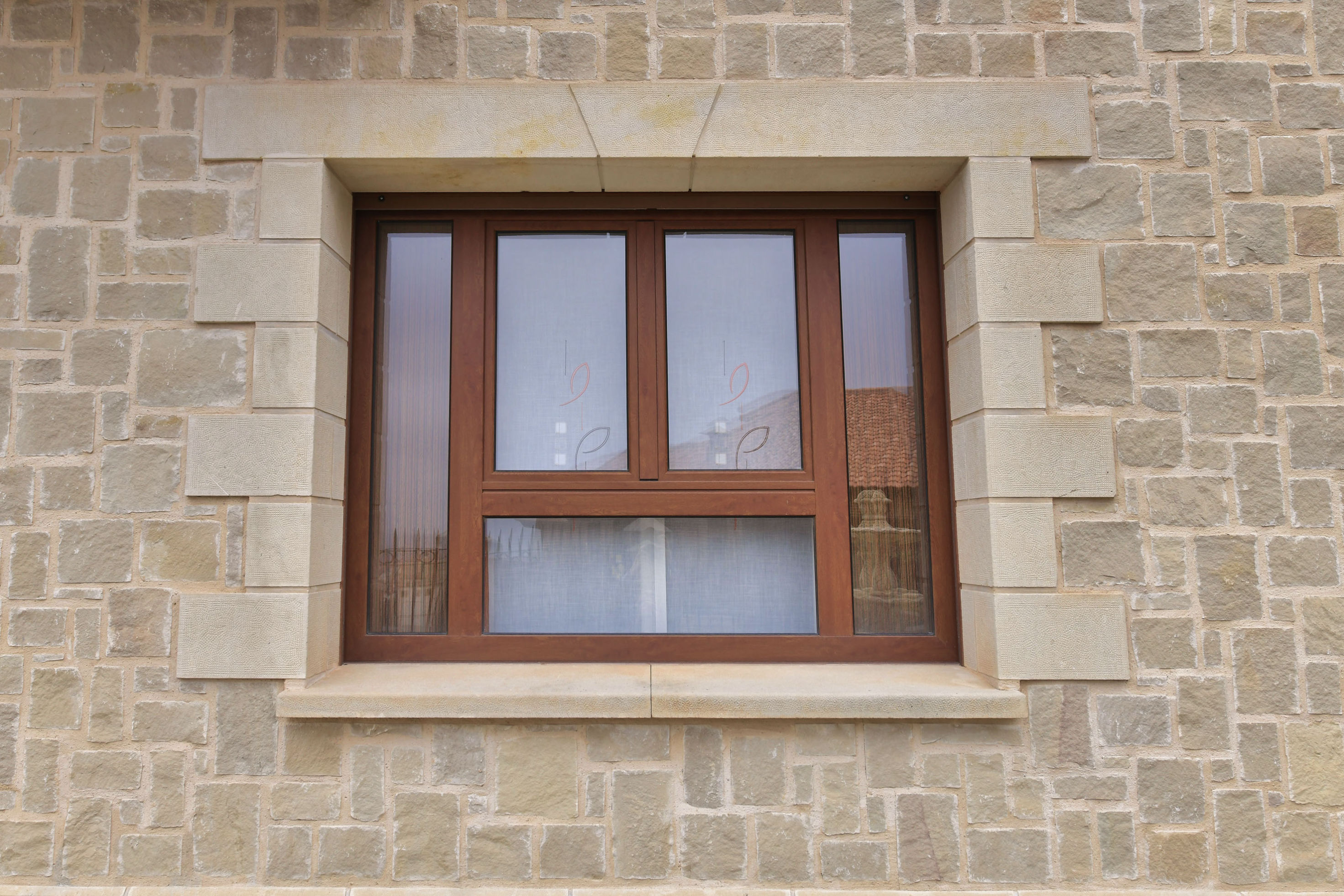 Ventanas de madera oscura con marco de piedra sobre fachada verde, con jardineras con flores
