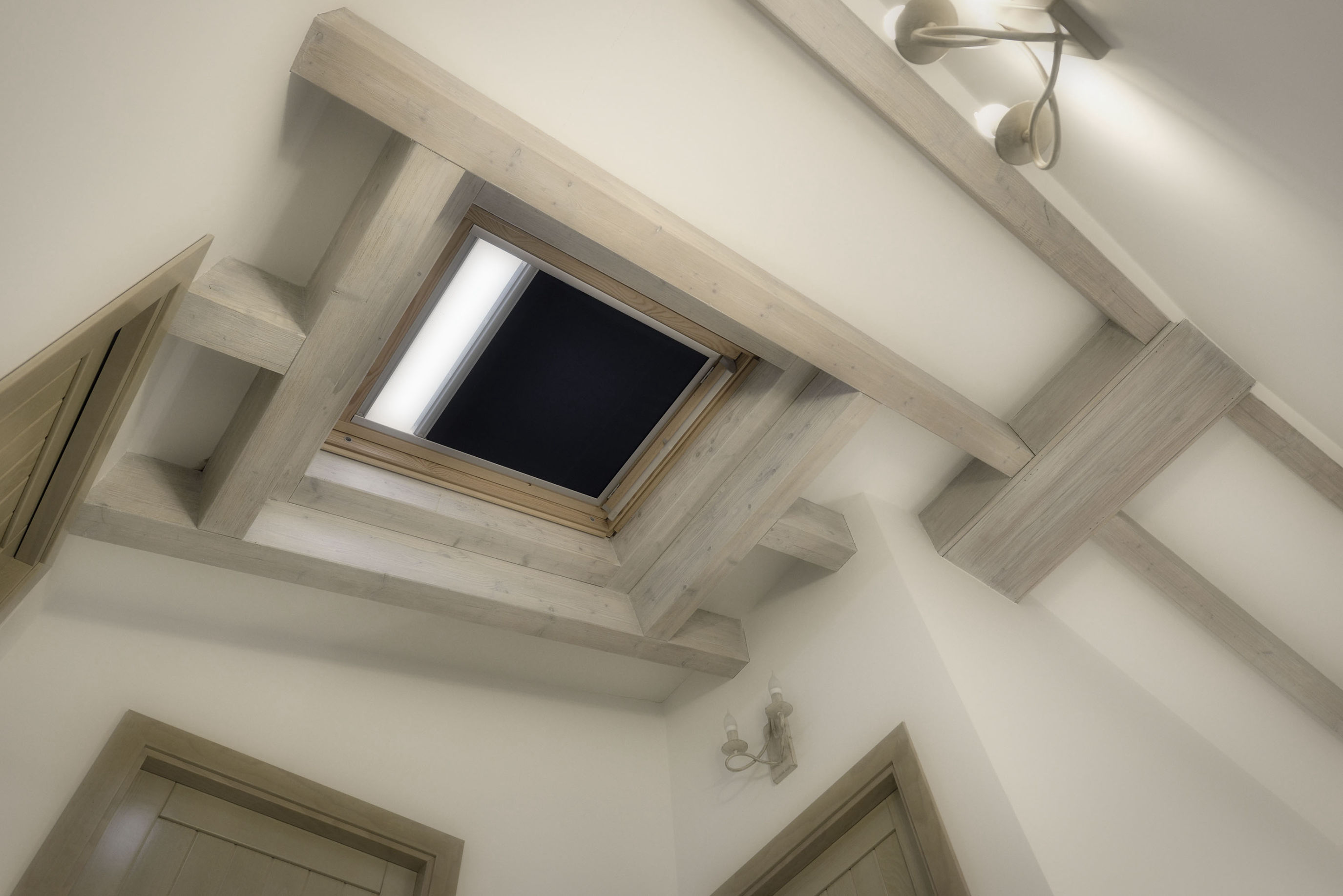 Vista interior de techo inclinado con vigas de madera clara y tragaluz central, en una estancia con acabados naturales y carpintería interior de estilo rústico.